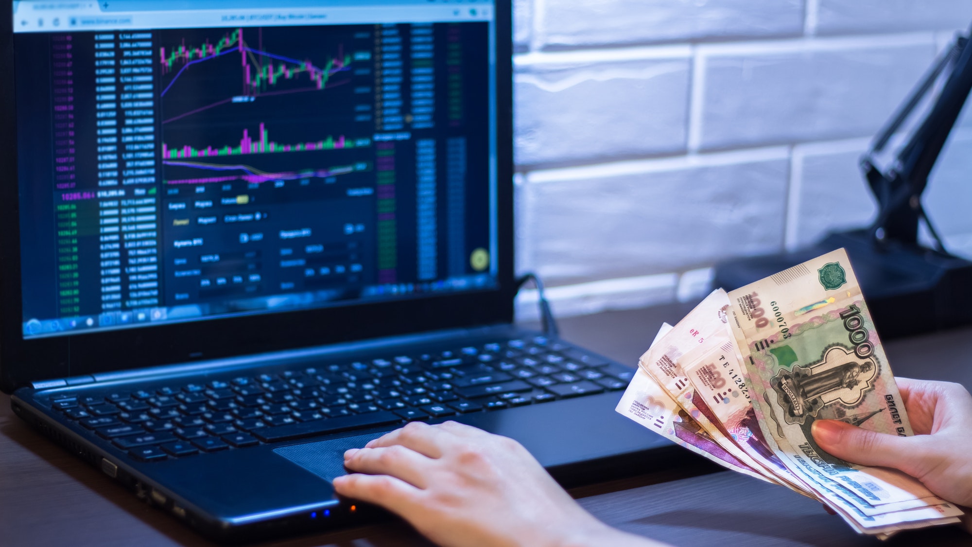 Hands holding Russian rubles in front of a computer monitor with the currency market and Forex